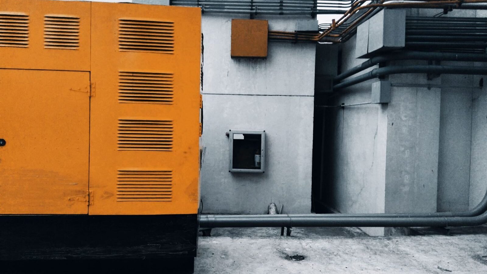 A large louvred standby generator enclosure on a pad outside a building