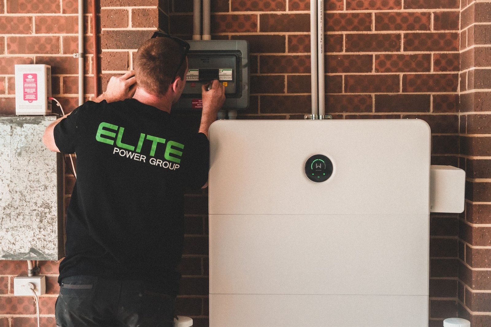 An electrician wiring an isolator beside a floor-standing home battery unit