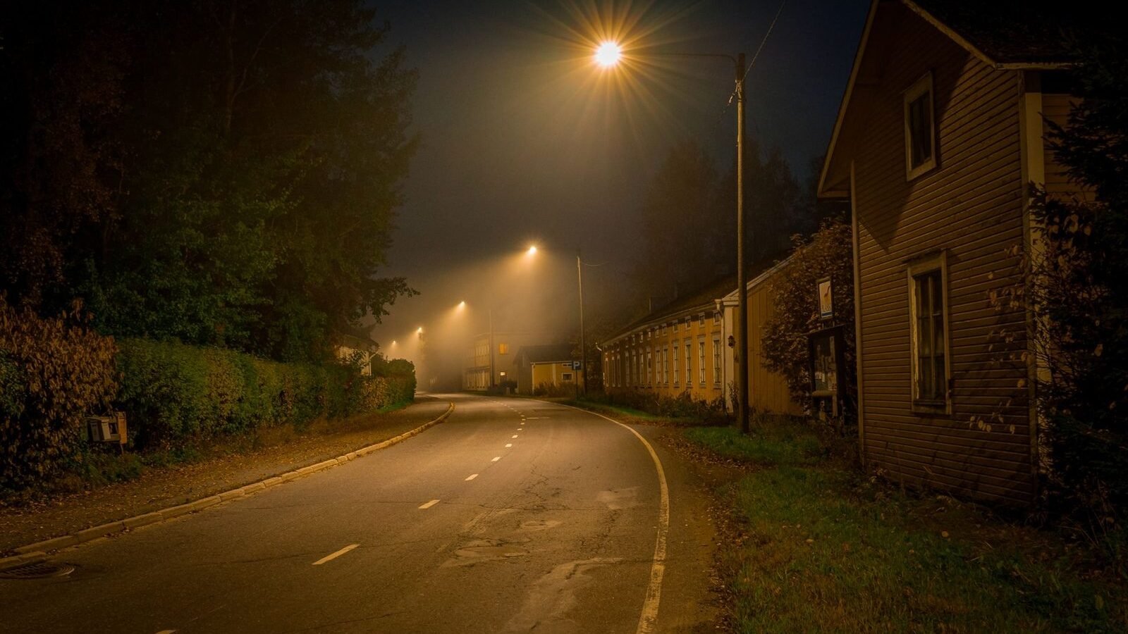 A dark residential street at night lit by a single streetlight