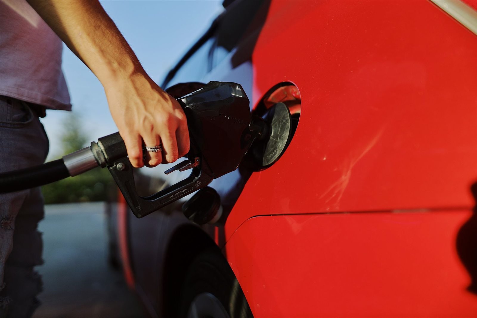 A person refuelling a red car at a filling station pump