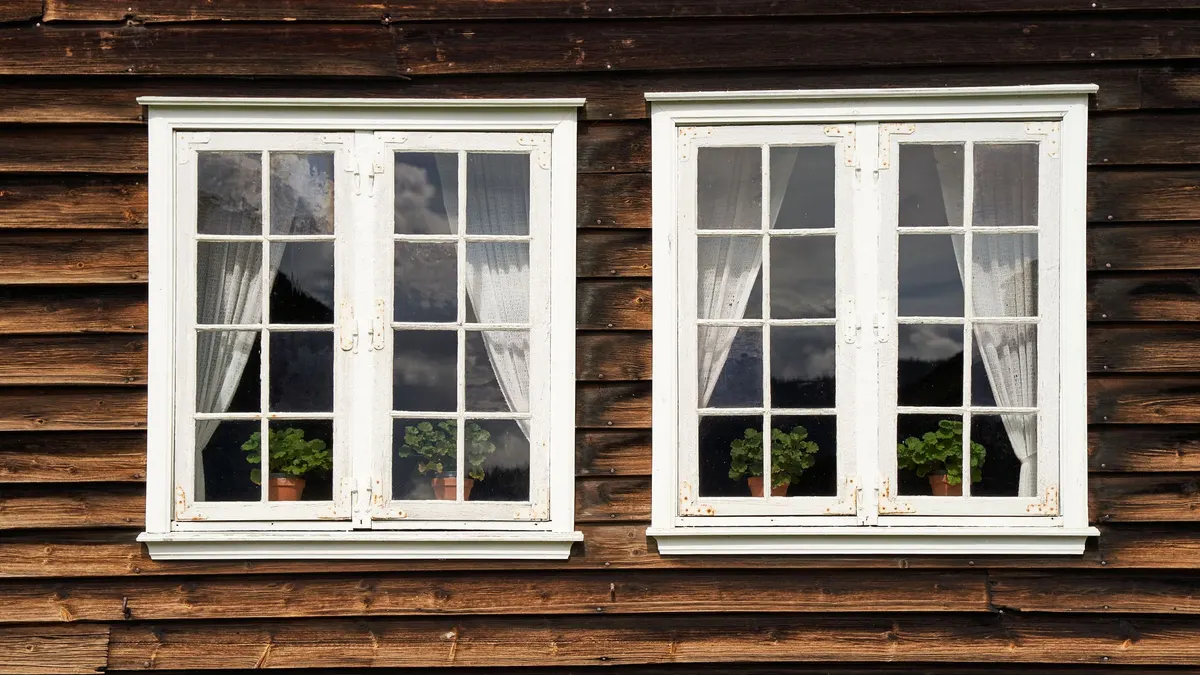 Two white windows in a wooden house wall