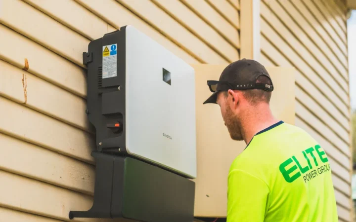 Installer next to a wall-mounted home battery system on a house exterior