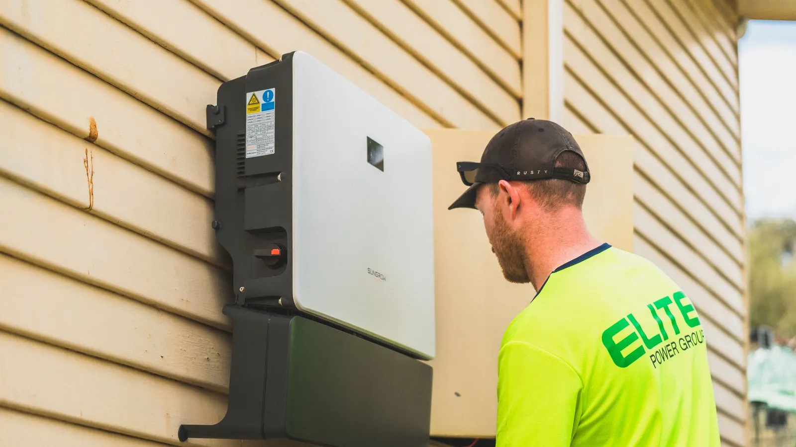 Installer next to a wall-mounted home battery system on a house exterior
