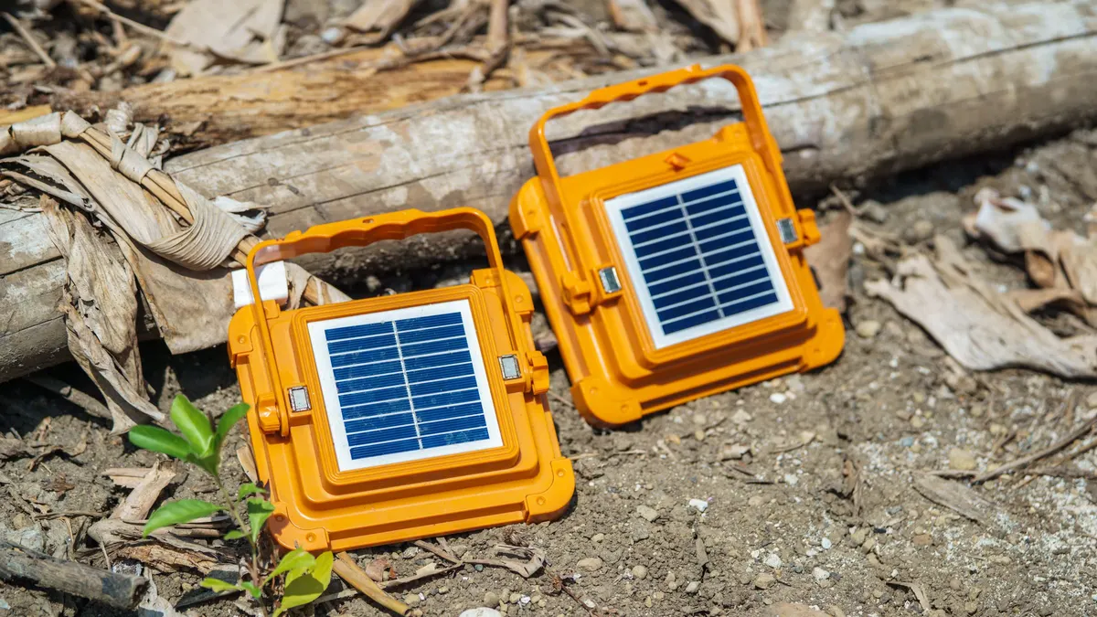 Two orange solar lanterns on dry ground outdoors