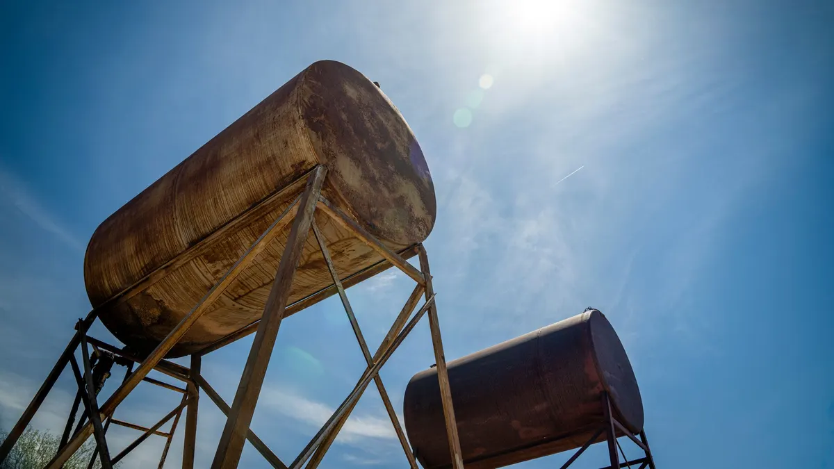 Weathered metal fuel tank on a stand against a blue sky
