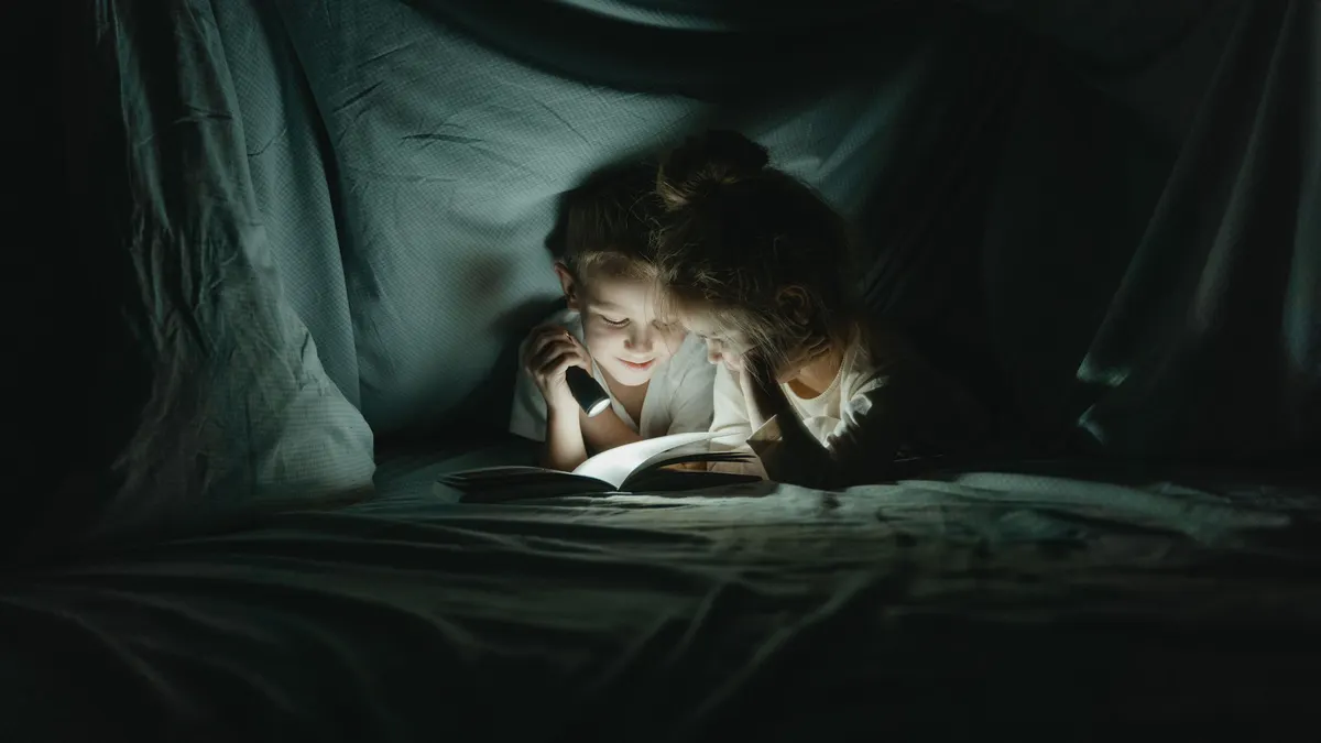 Child reading by flashlight under a blanket