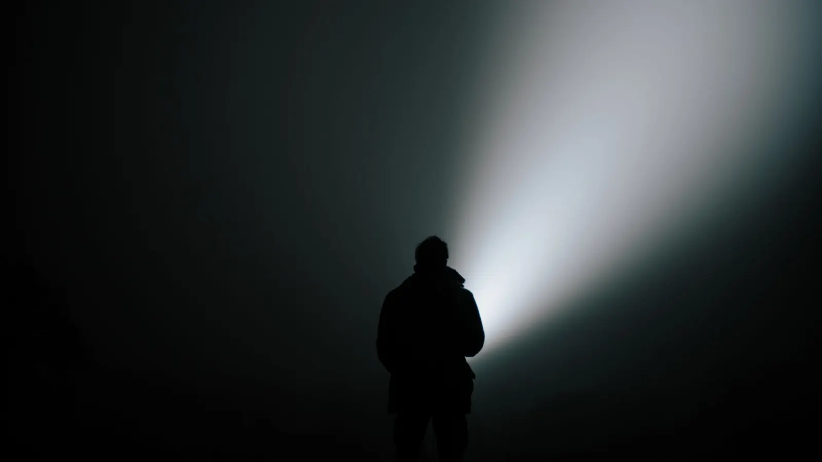 Person shining a flashlight beam in a dark room