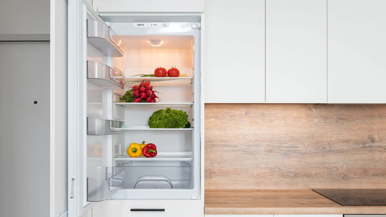Open refrigerator with vegetables in a bright kitchen