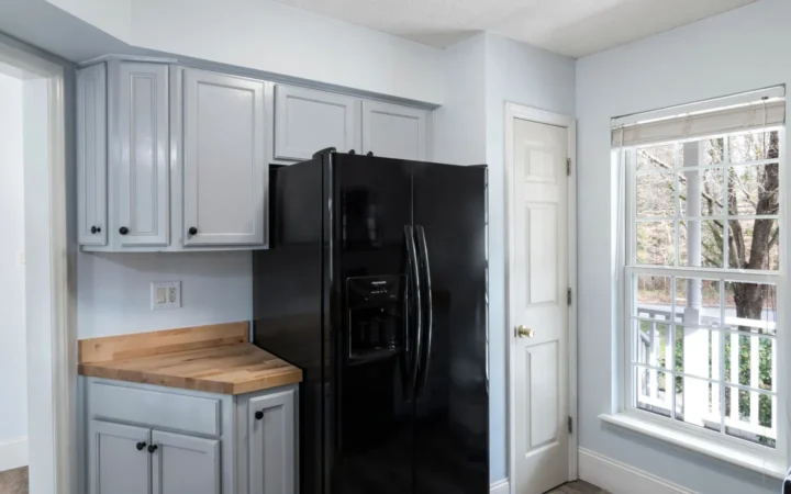 Black refrigerator in a white kitchen beside a window