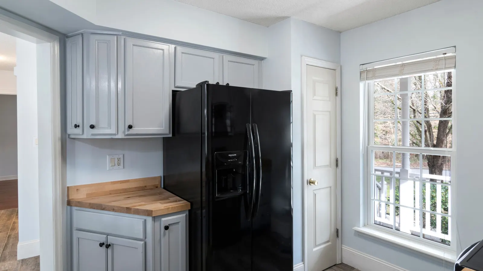 Black refrigerator in a white kitchen beside a window