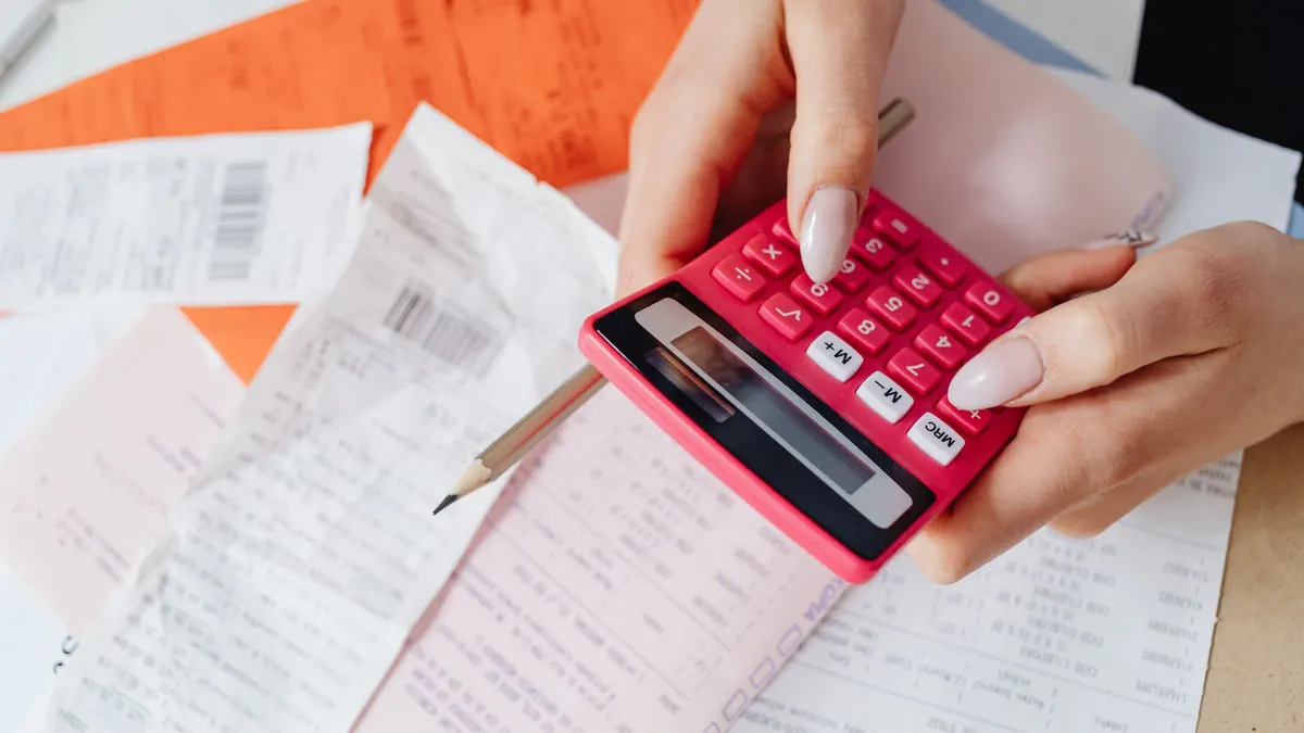 Hands using a pink calculator over paper bills