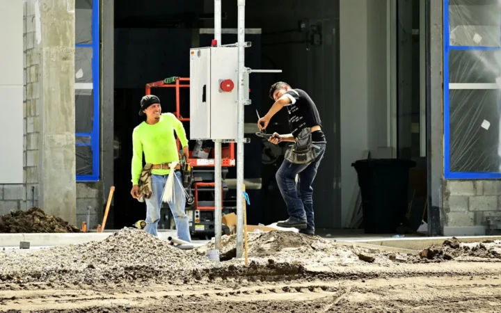 Two workers installing an electrical panel outdoors at a building site