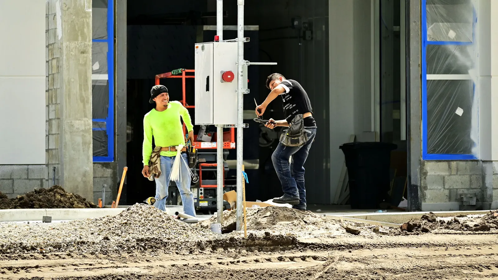Two workers installing an electrical panel outdoors at a building site