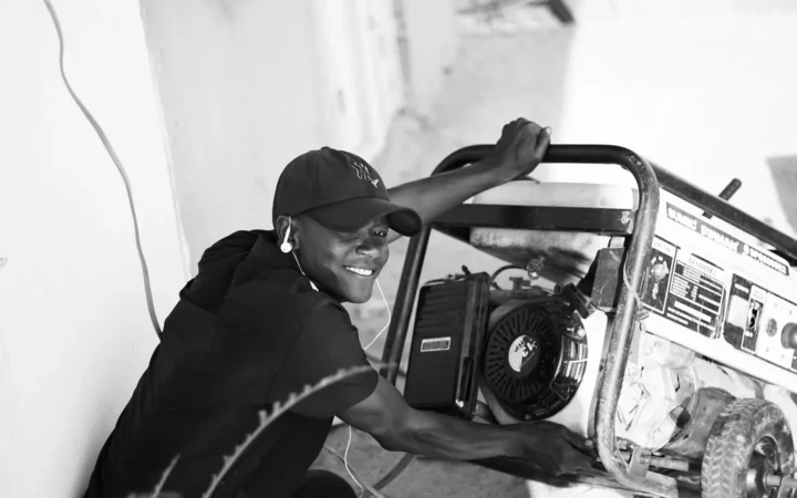 Man kneeling beside a portable generator outdoors, black and white photo