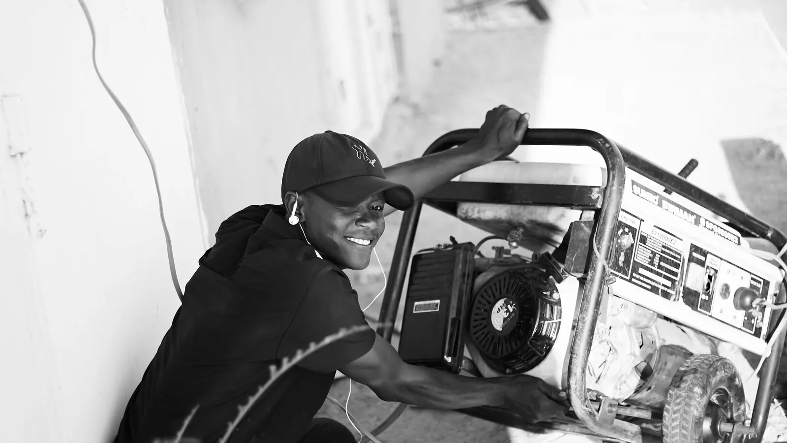 Man kneeling beside a portable generator outdoors, black and white photo
