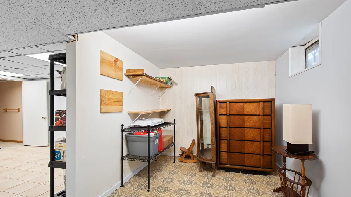 Clean basement room with shelving and a wooden cabinet