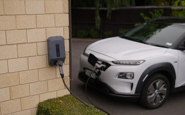 White electric SUV charging from a wall-mounted charger outside a house