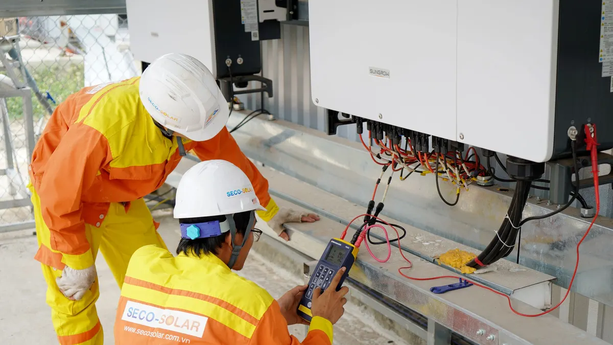 Two technicians testing an inverter mounted on a wall
