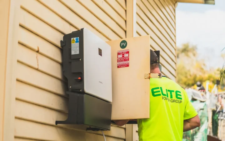 Home battery unit mounted on yellow house siding with an installer nearby
