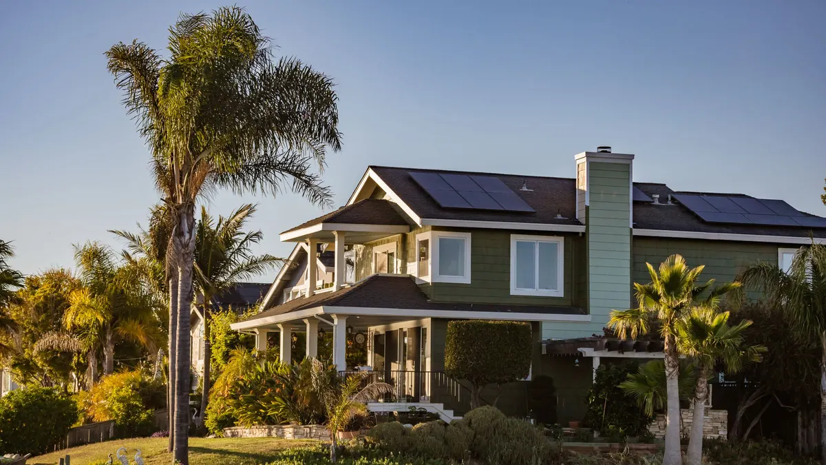 Two-story house with rooftop solar surrounded by palm trees
