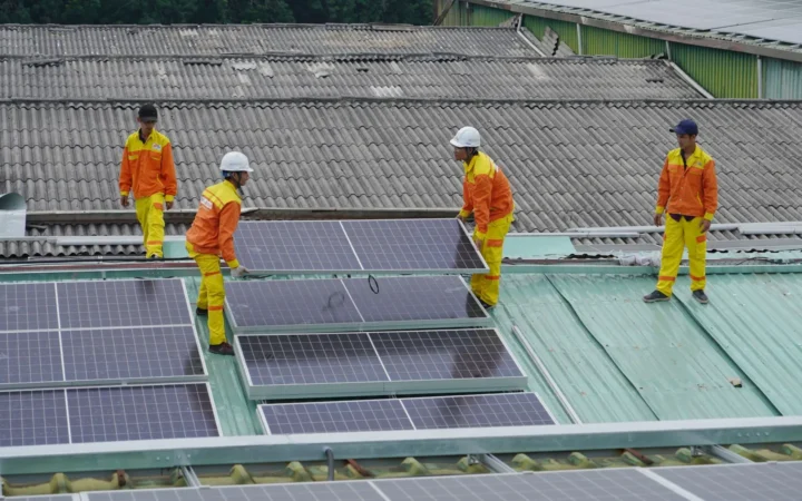 Workers in orange safety gear installing solar panels on a roof