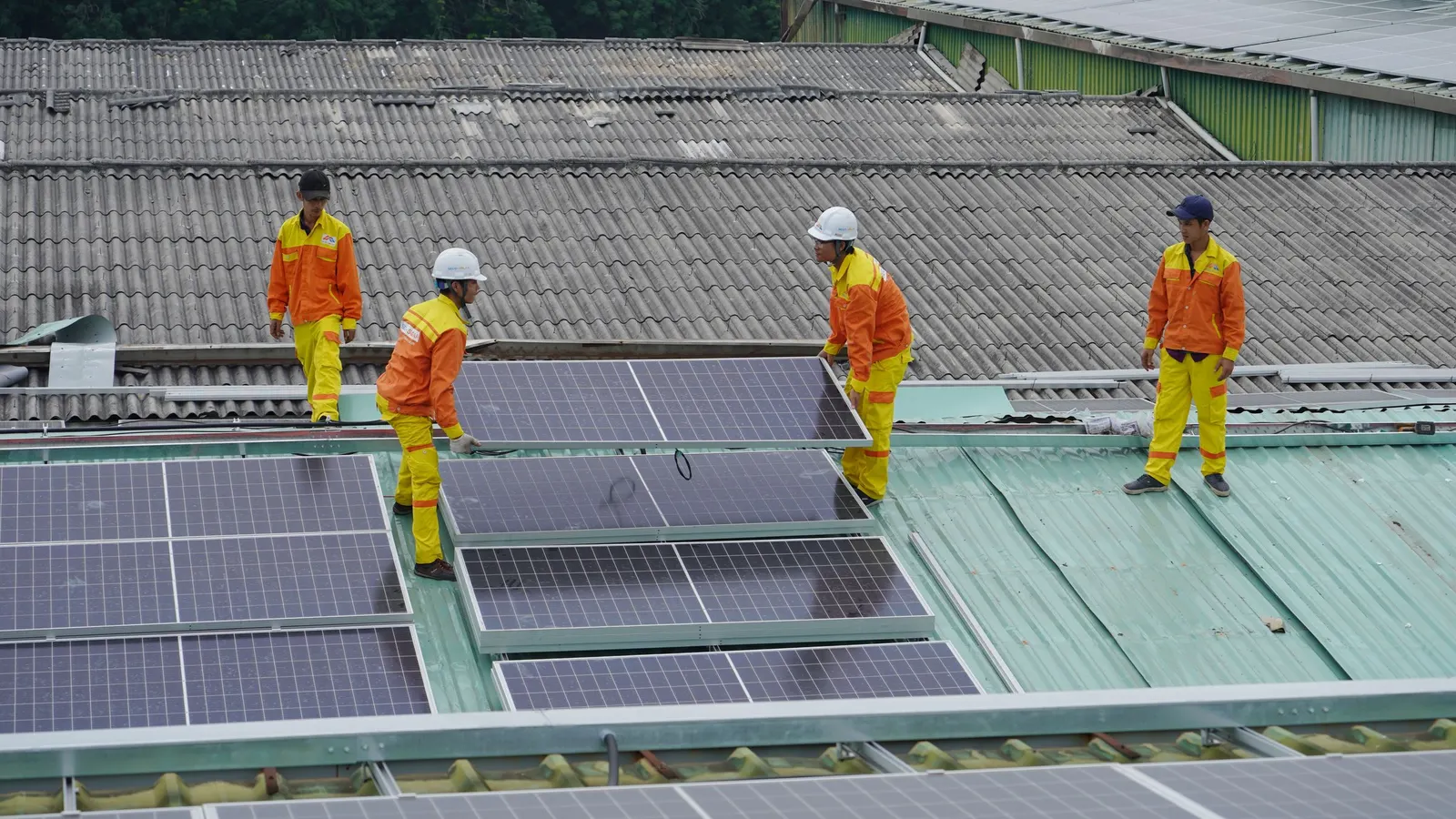 Workers in orange safety gear installing solar panels on a roof