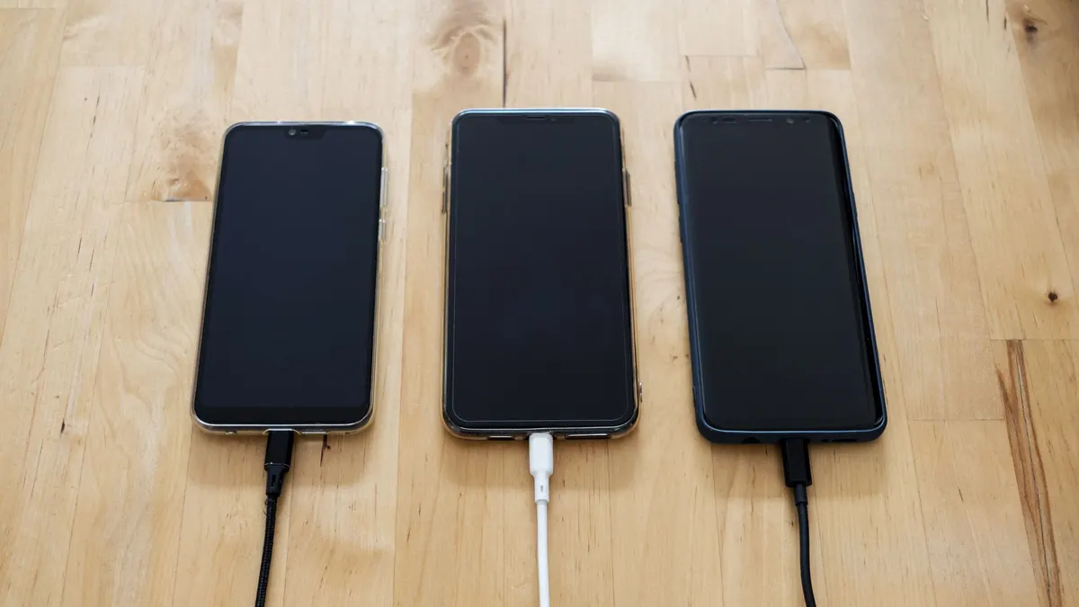 Three smartphones charging on a wooden table