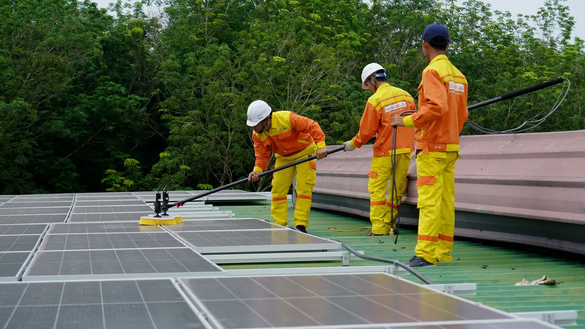Workers in safety gear cleaning a rooftop solar array