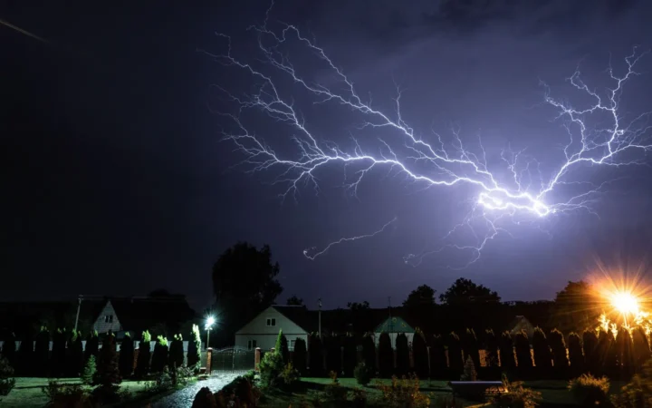 Lightning striking above houses and street lights at night