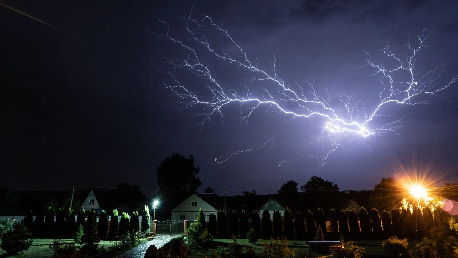 Lightning striking above houses and street lights at night