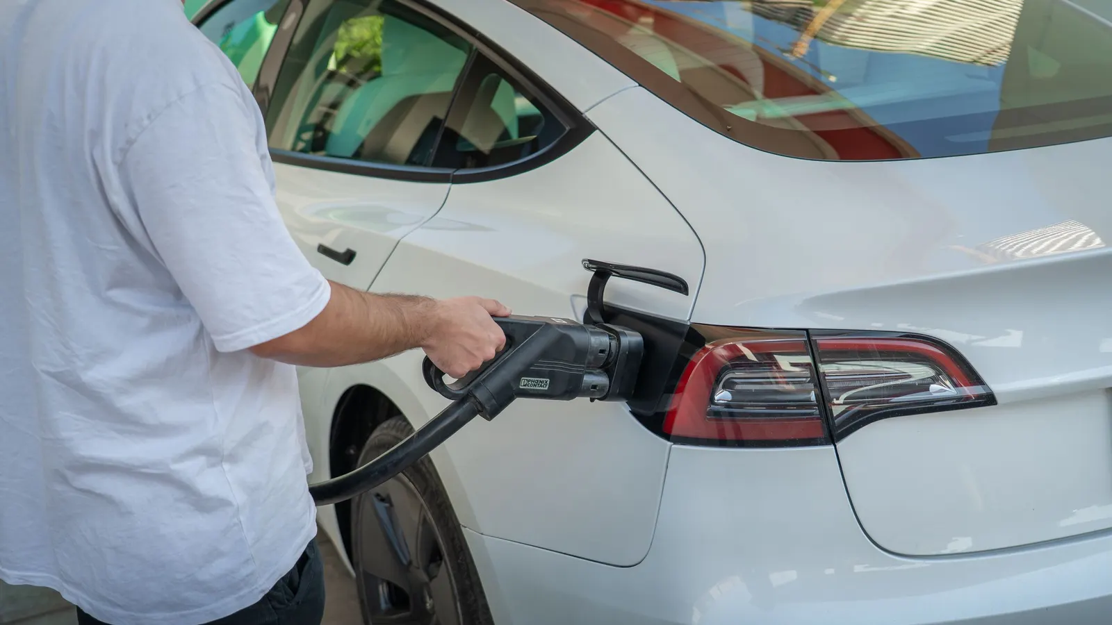 Man plugging a charging connector into a white electric car